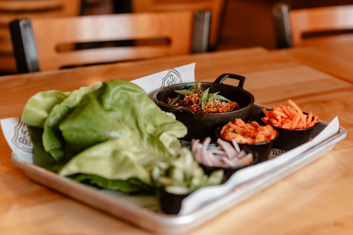 Fresh lettuce wraps served with kimchi, onions and seasoned meat on a metal tray at a wooden restaurant table.