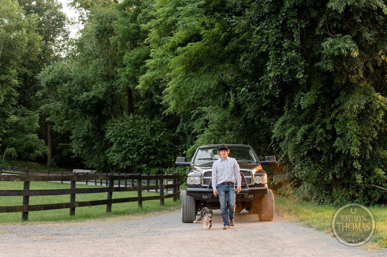 A person walks with their small dog on a gravel road near a parked black truck.