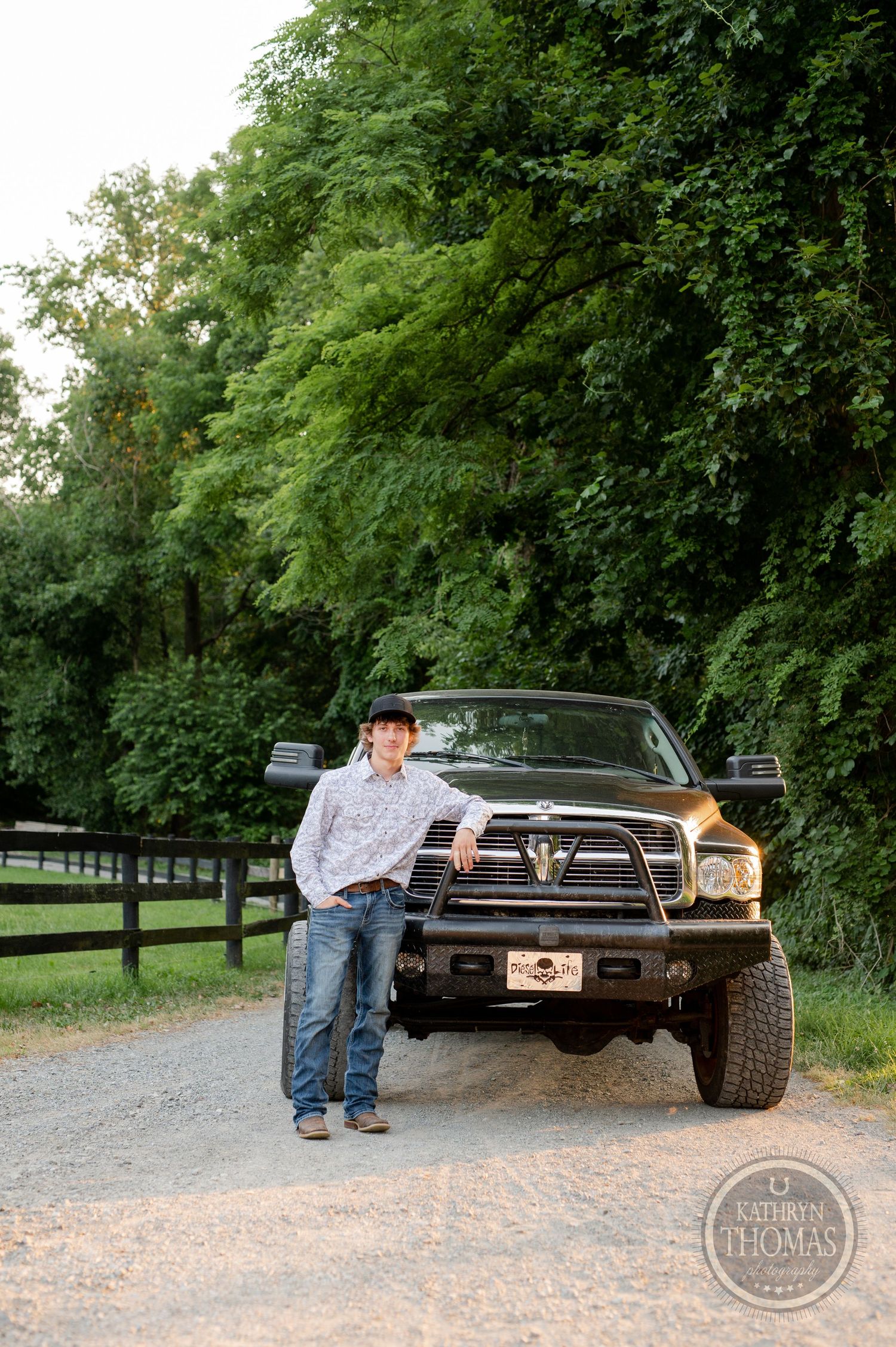 A lifted black Dodge Ram truck parked on a tree-lined gravel path near wooden fences.