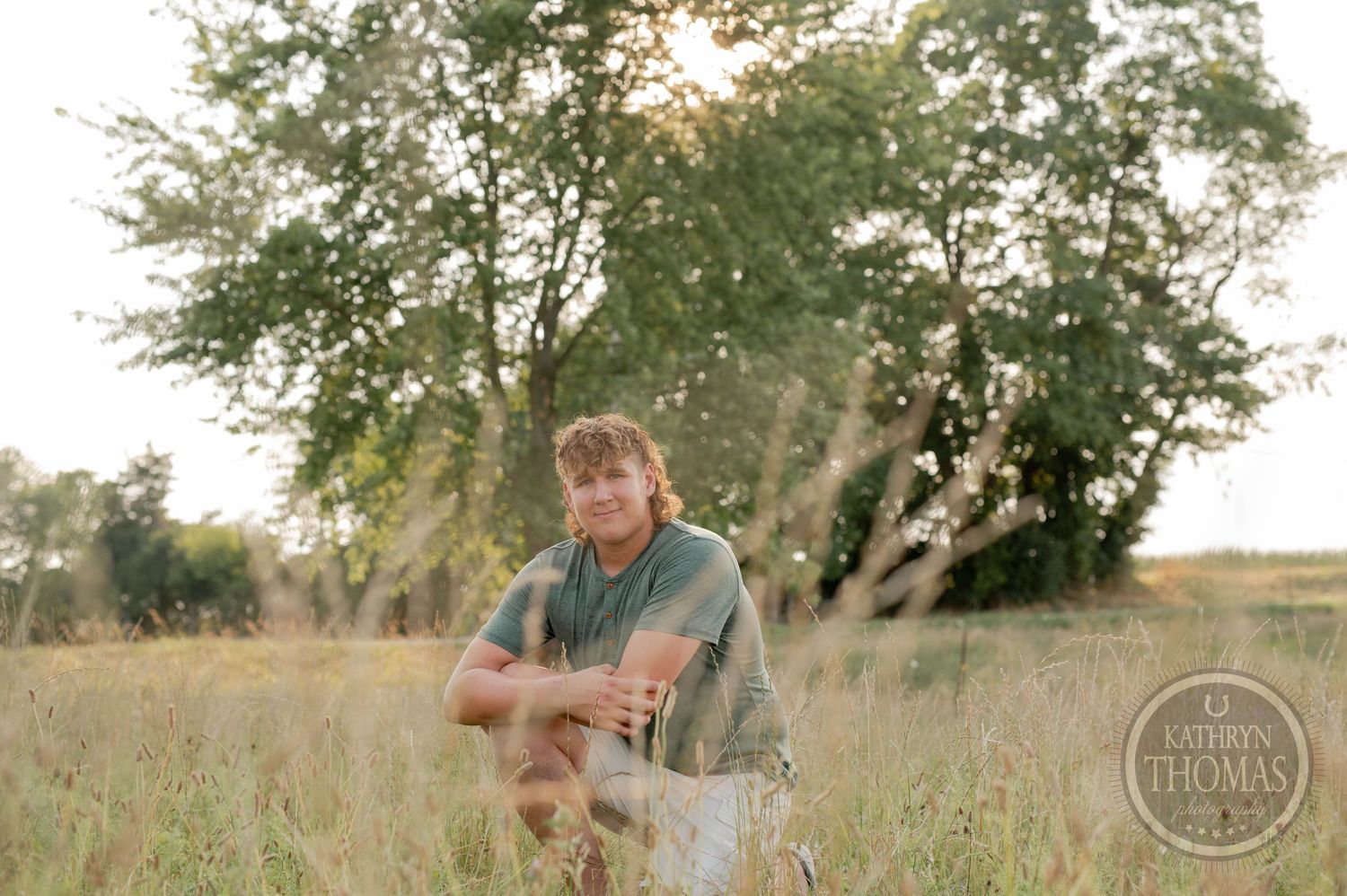 Person rests in tall grass with sunlit trees in the background.