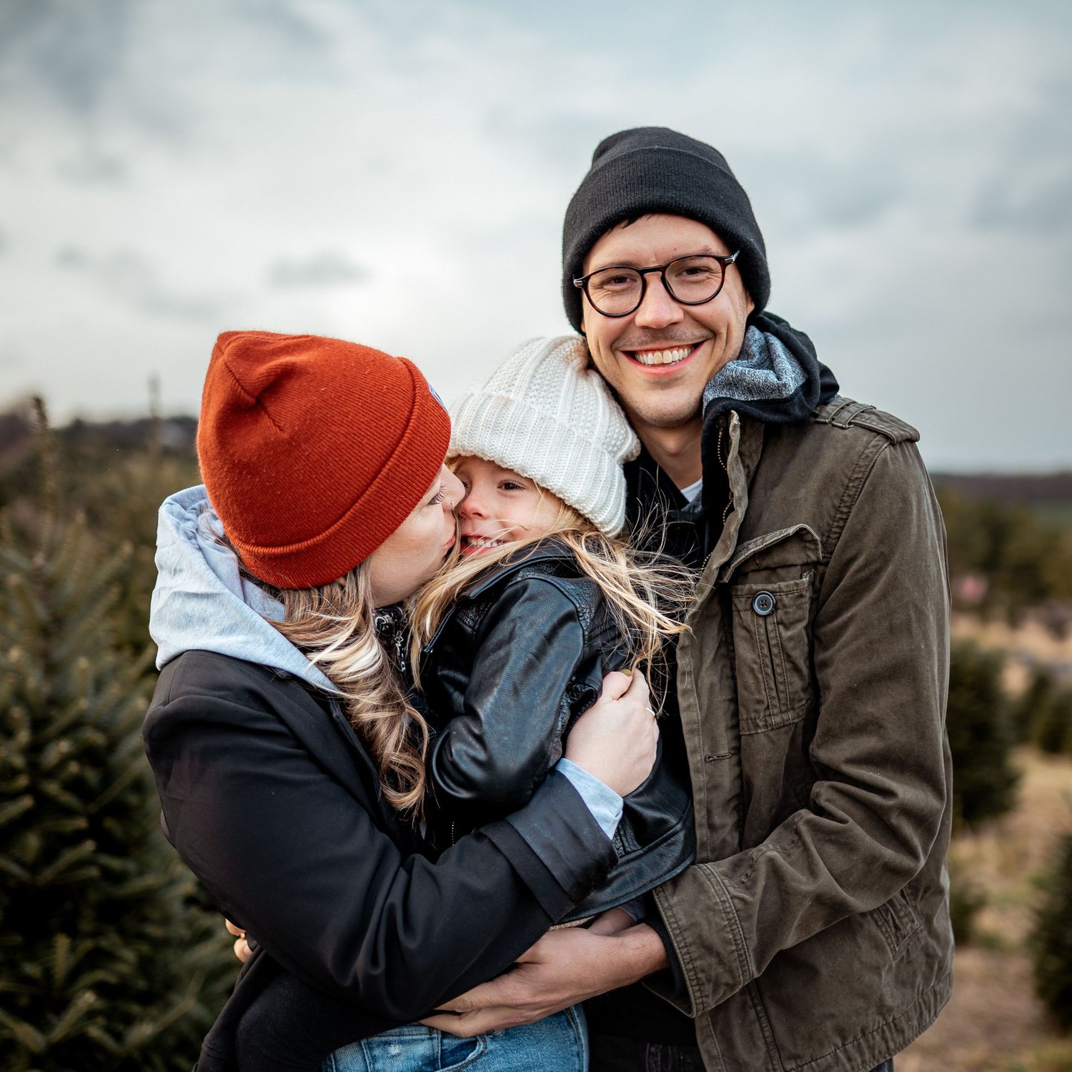 Family shares a tender moment while visiting a Christmas tree farm on an overcast winter day.