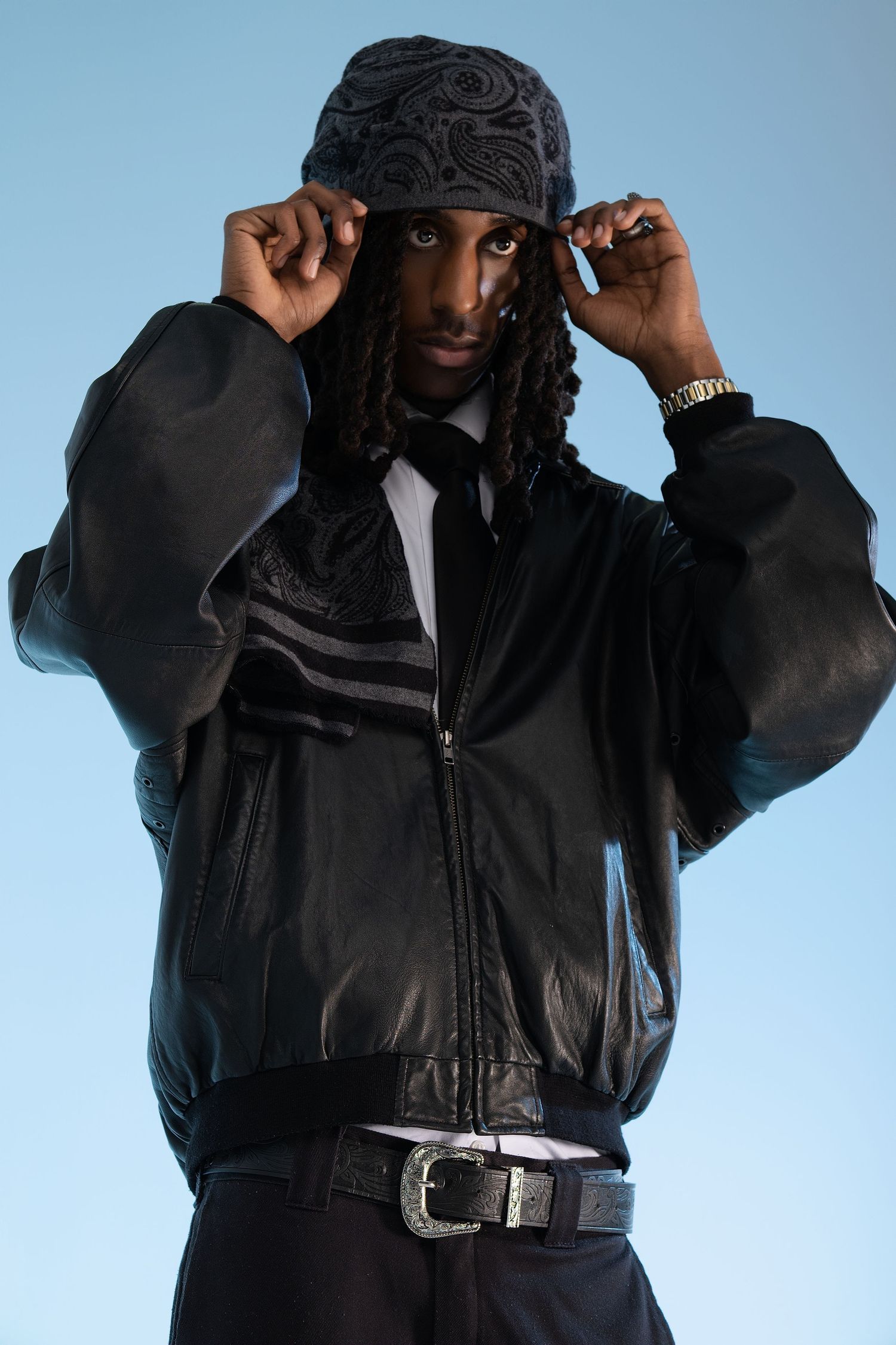 A person wearing a black puffy jacket and black beanie adjusts their hat against a blue background.