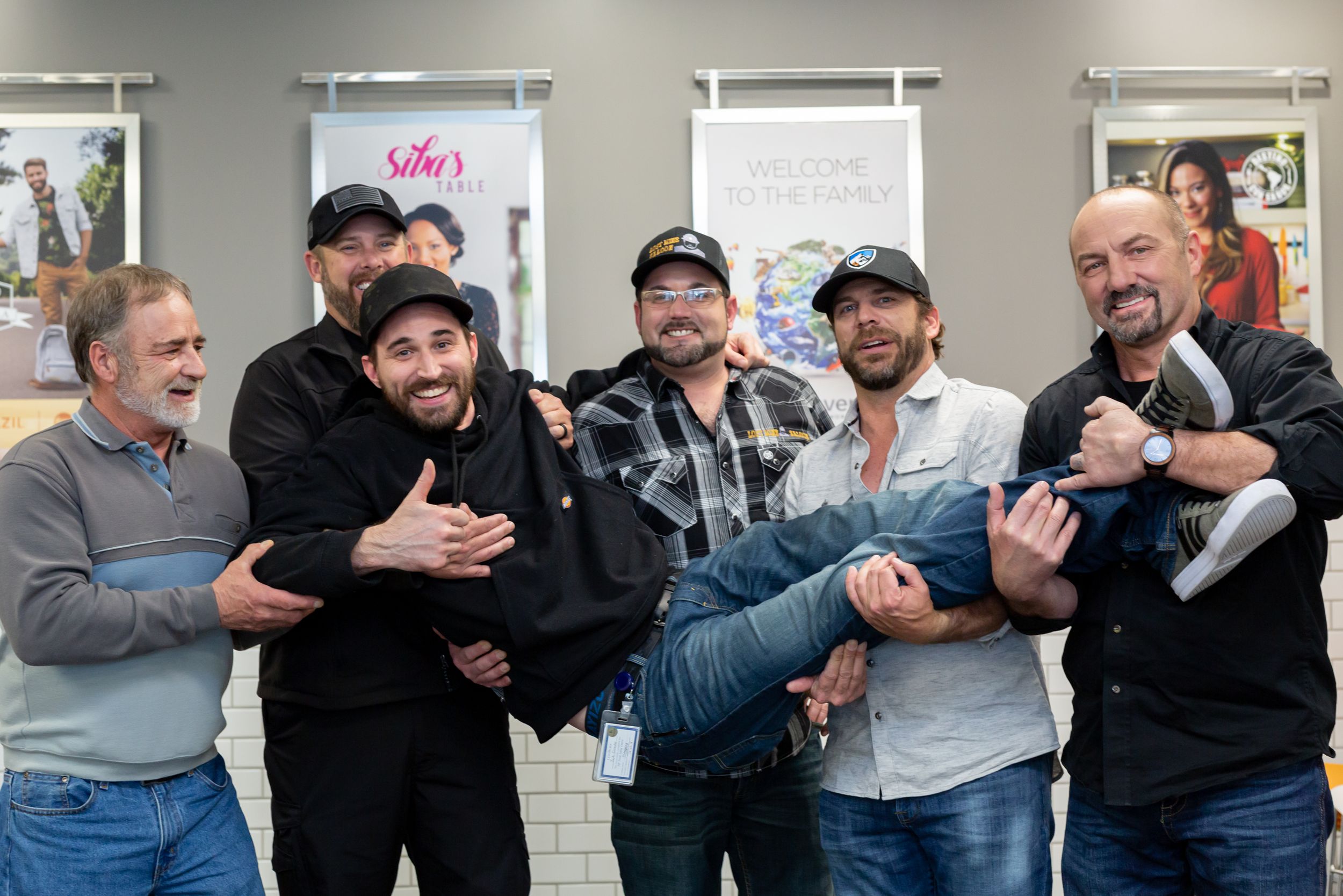 A group of five people having fun and laughing together while posing playfully outside a storefront.