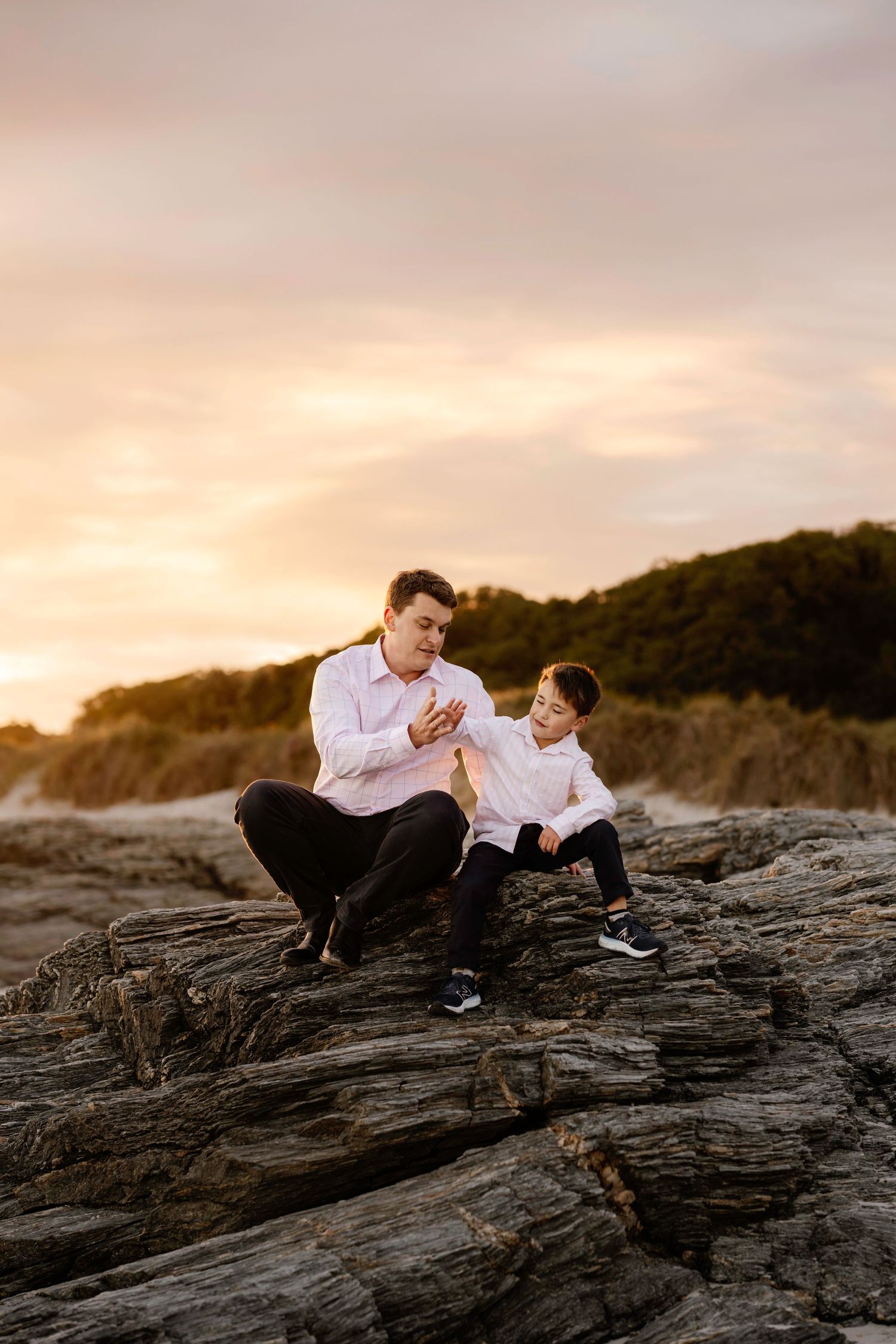 A tender family portrait shows parents in white embracing their newborn baby in a warm, intimate setting.