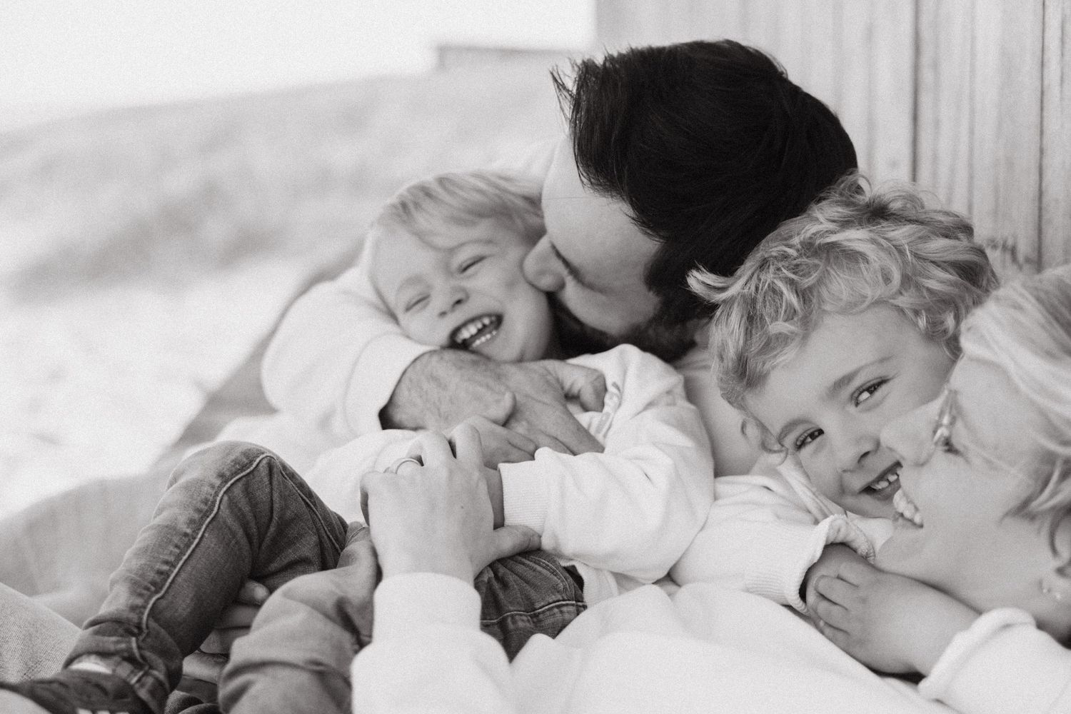 Sweet black and white photo of a tender family moment with children and parent snuggling together in bed.