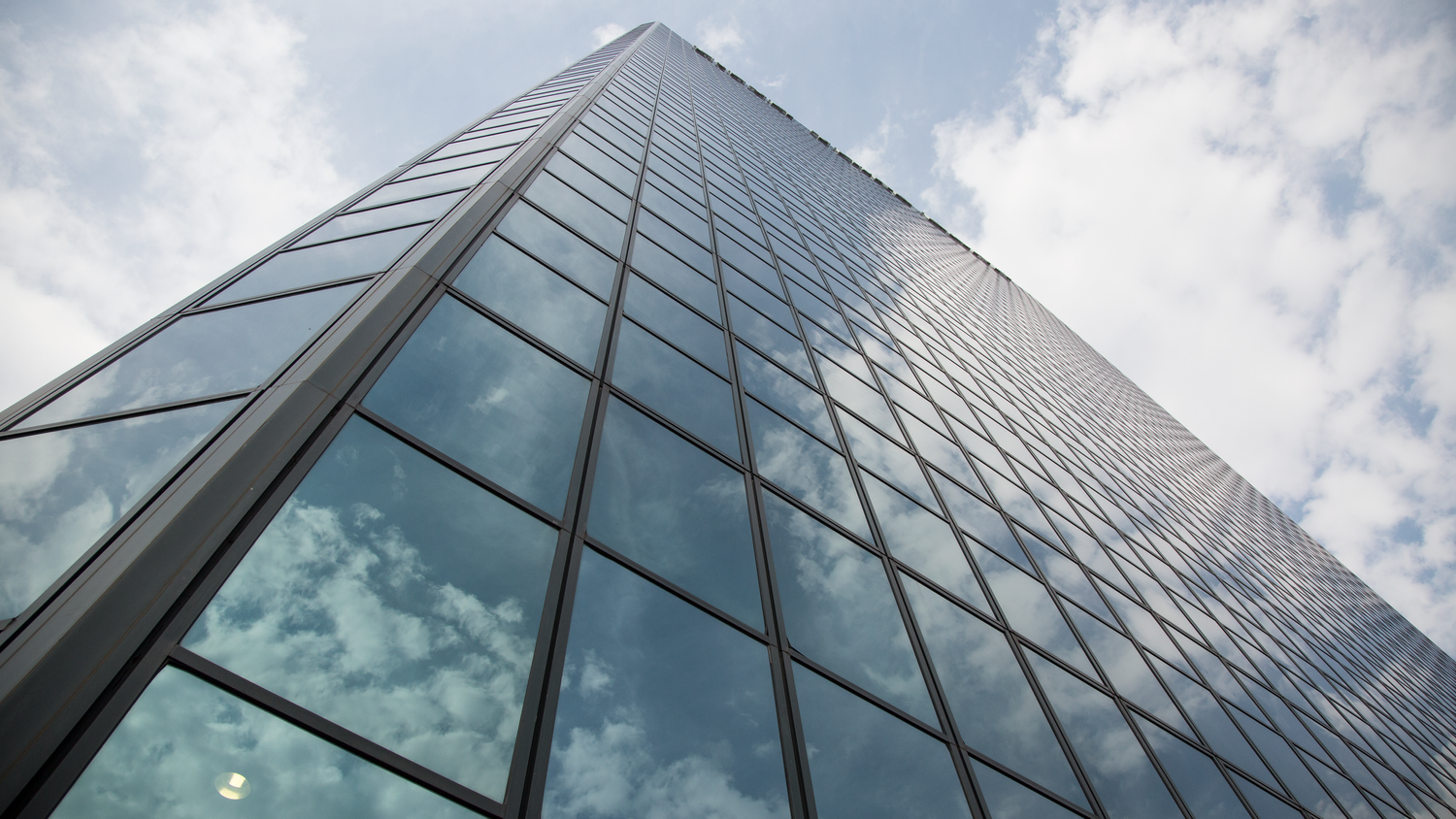 Modern glass skyscraper reflecting clouds and sky from a dramatic low angle perspective.