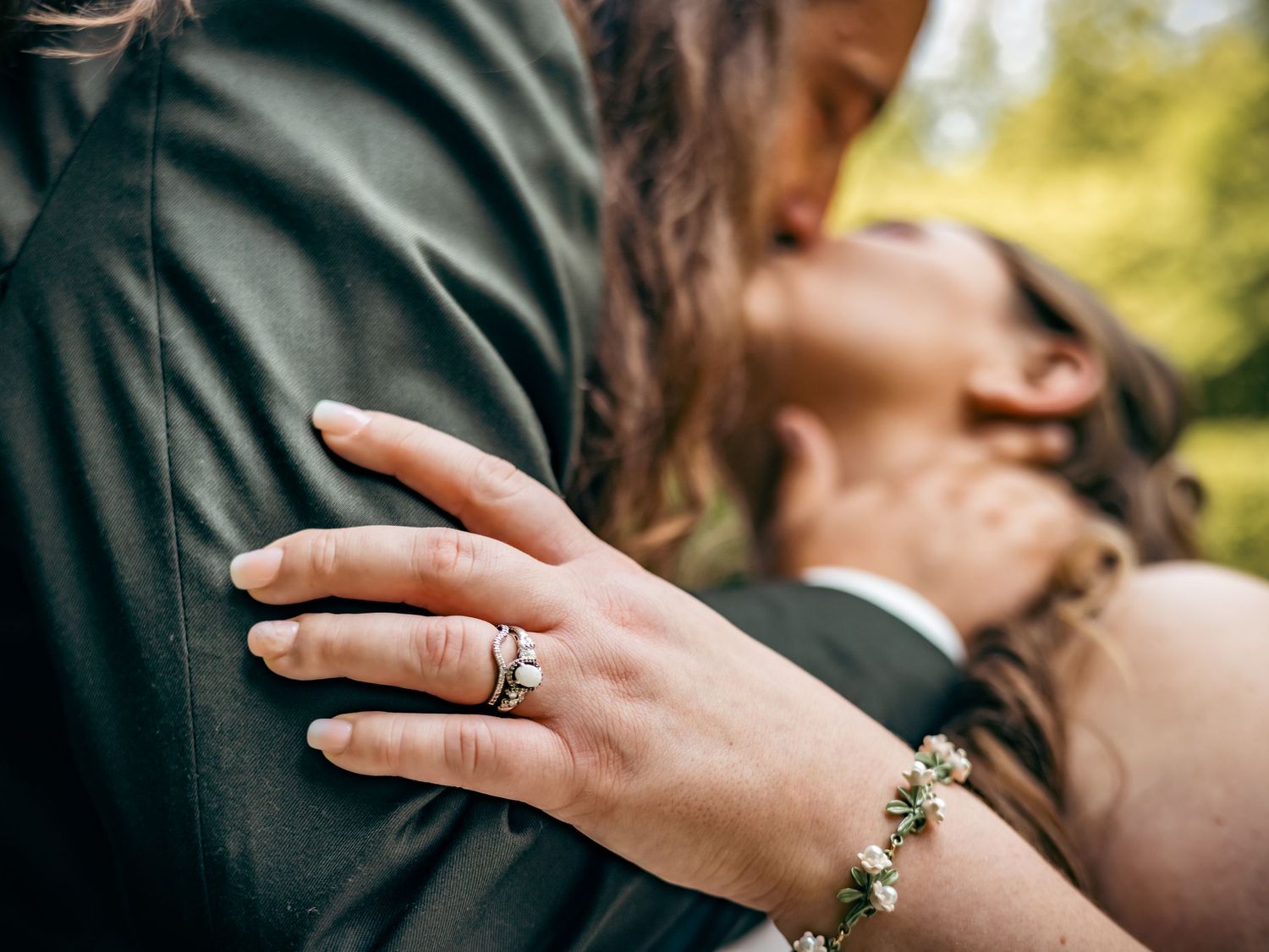 Close-up of an engagement ring and bracelet as a couple embraces.