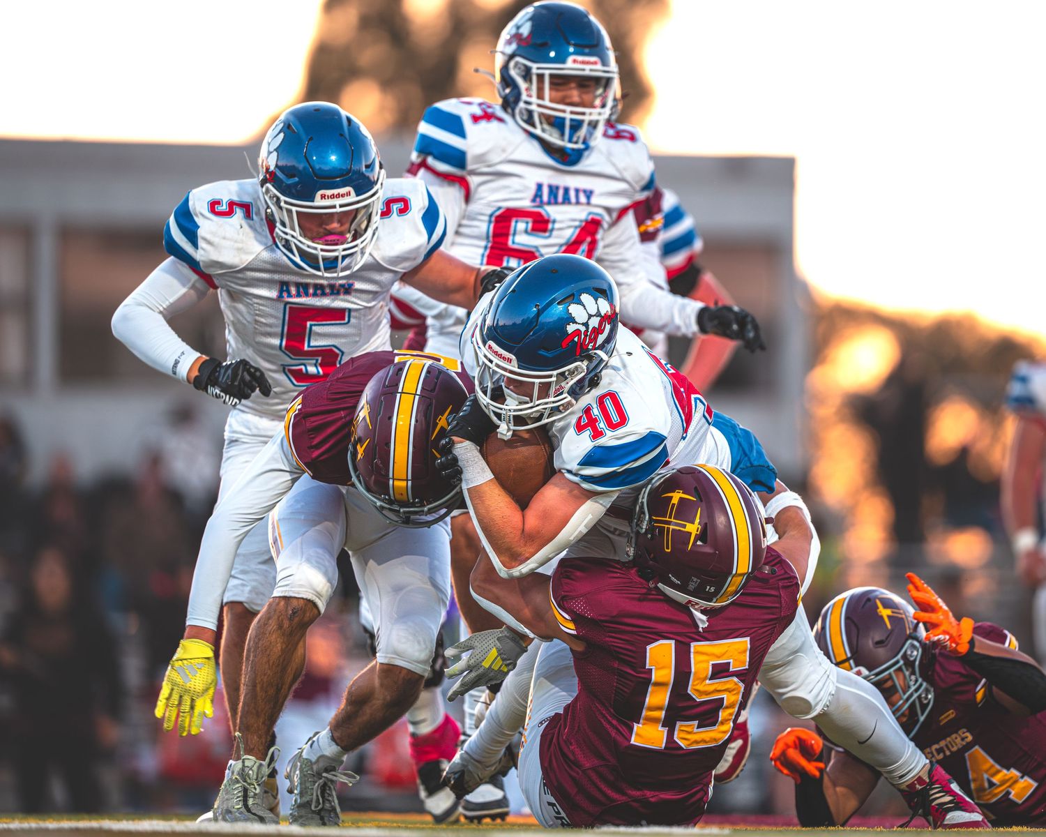 Football players collide in a high school game as defenders tackle the ball carrier during an intense play.