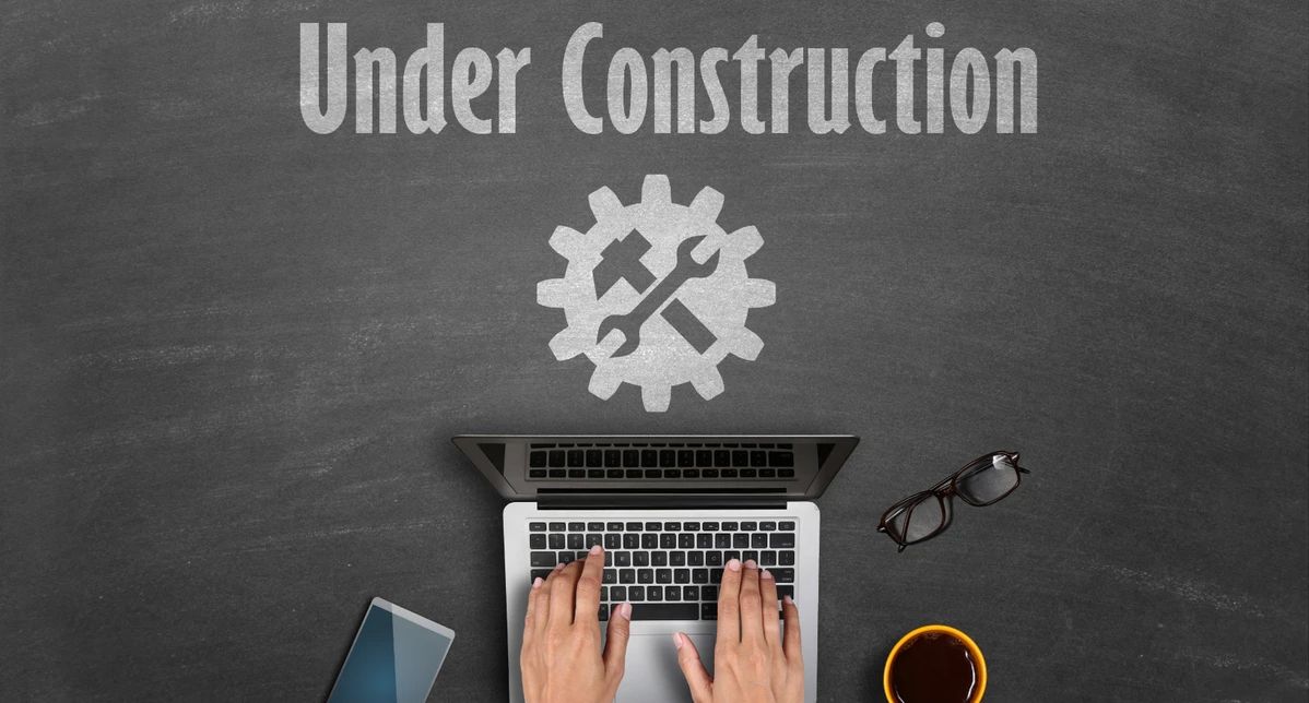 Overhead view of laptop with 'Under Construction' text and gear icon on chalkboard background.