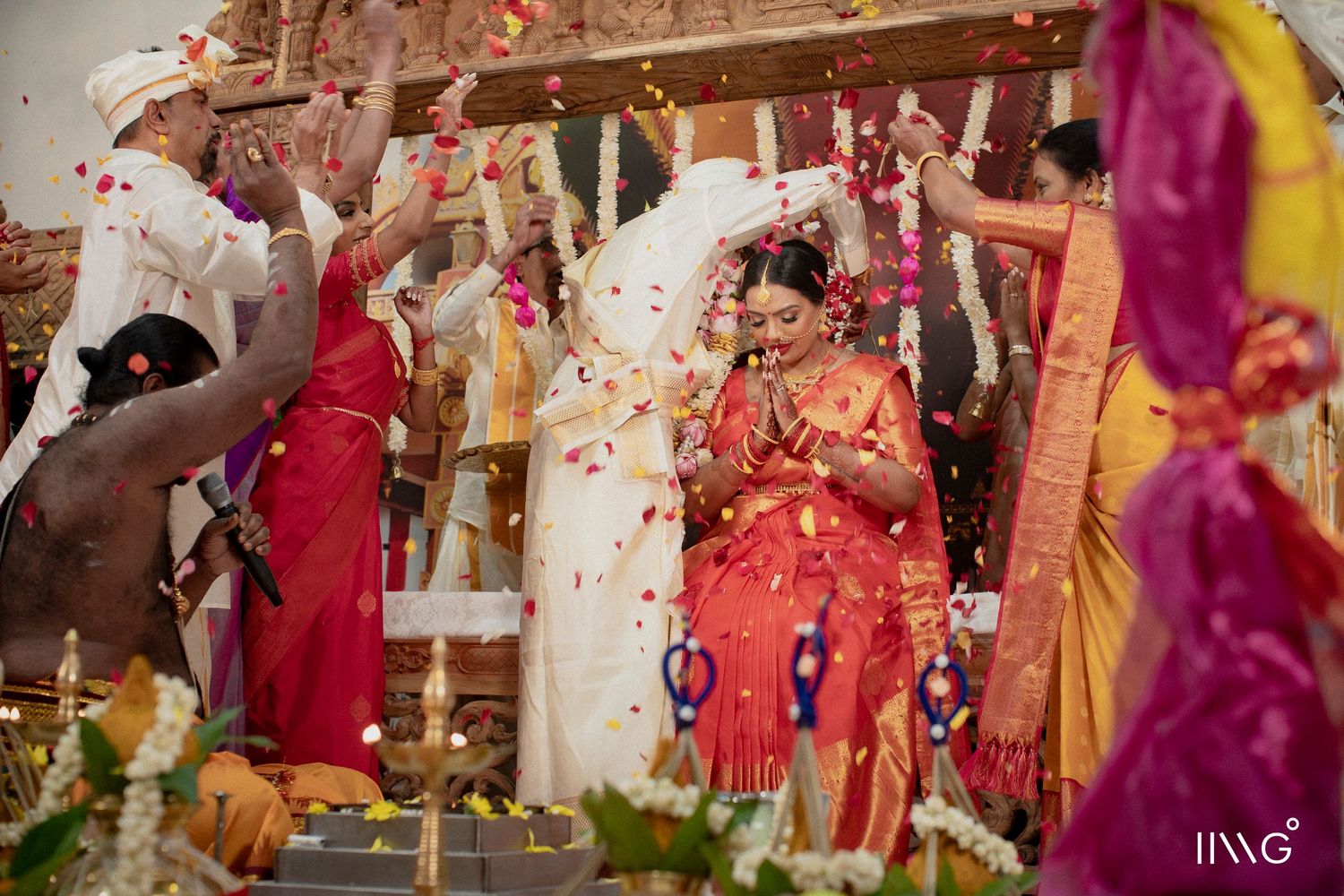Wedding celebration with flower petals being showered on guests in colorful traditional attire at a decorated ceremony venue.