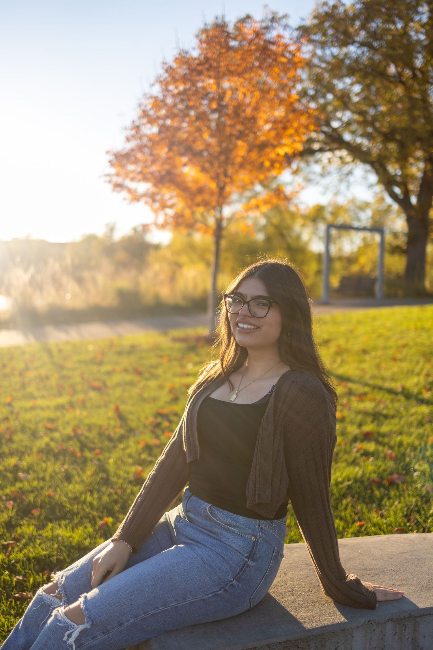Woman in blue jumpsuit with curly hair smiles while standing on a forest path at sunset.