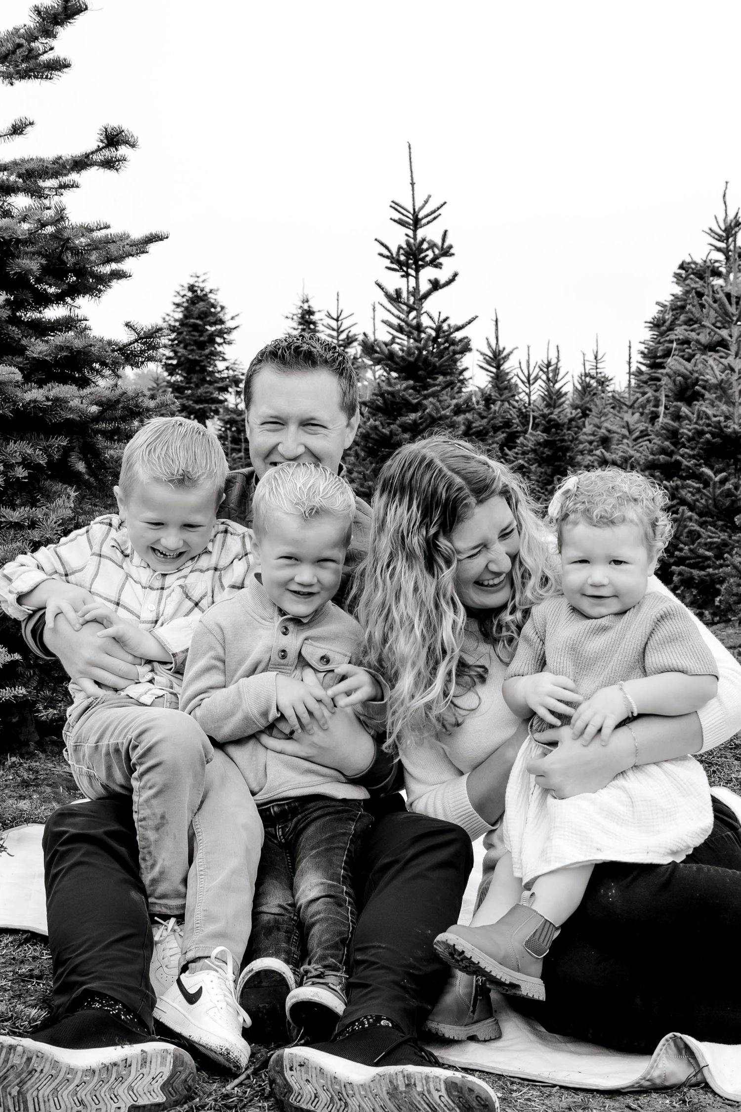 Black and white photo of a joyful family of five laughing together at a Christmas tree farm.