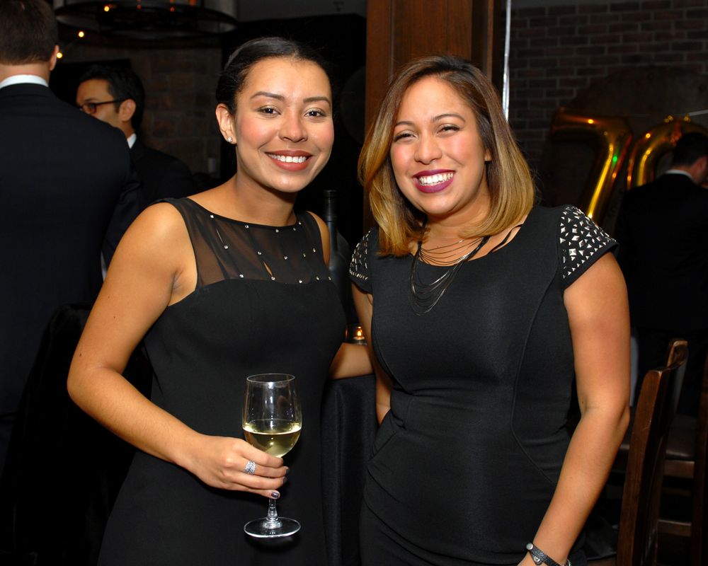 Two women in black dresses at formal event holding wine glasses.