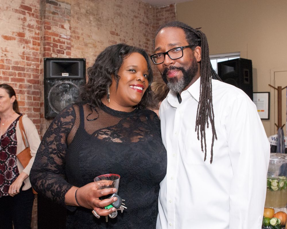 A couple at social gathering in formal attire against brick wall background.