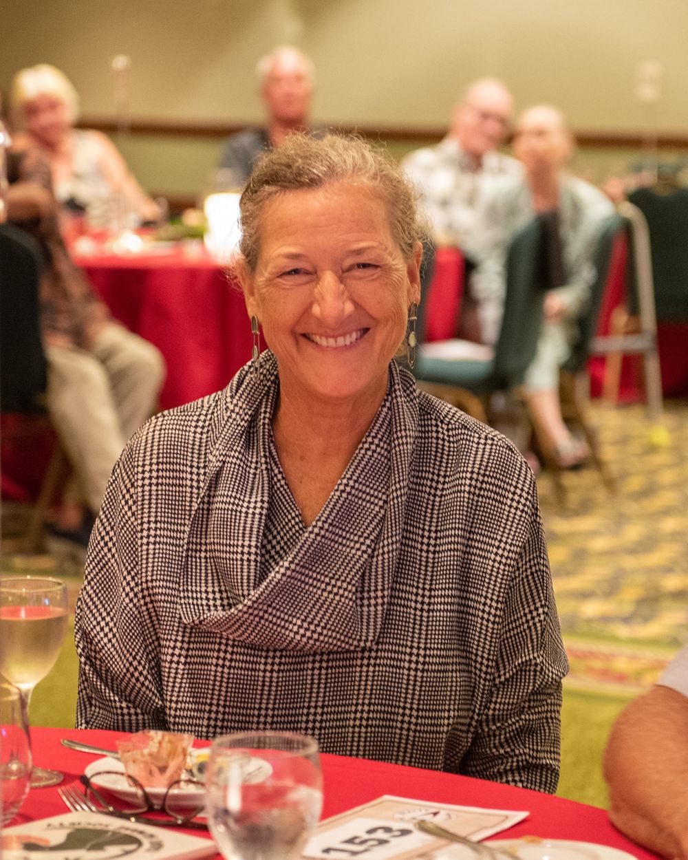 Person in plaid shirt seated at round banquet table during formal event.