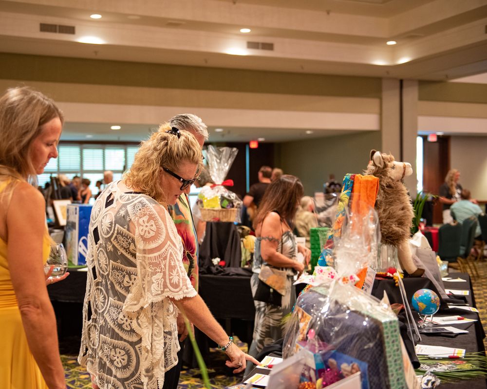 People browsing items at a charity auction table displaying various gift baskets and merchandise.