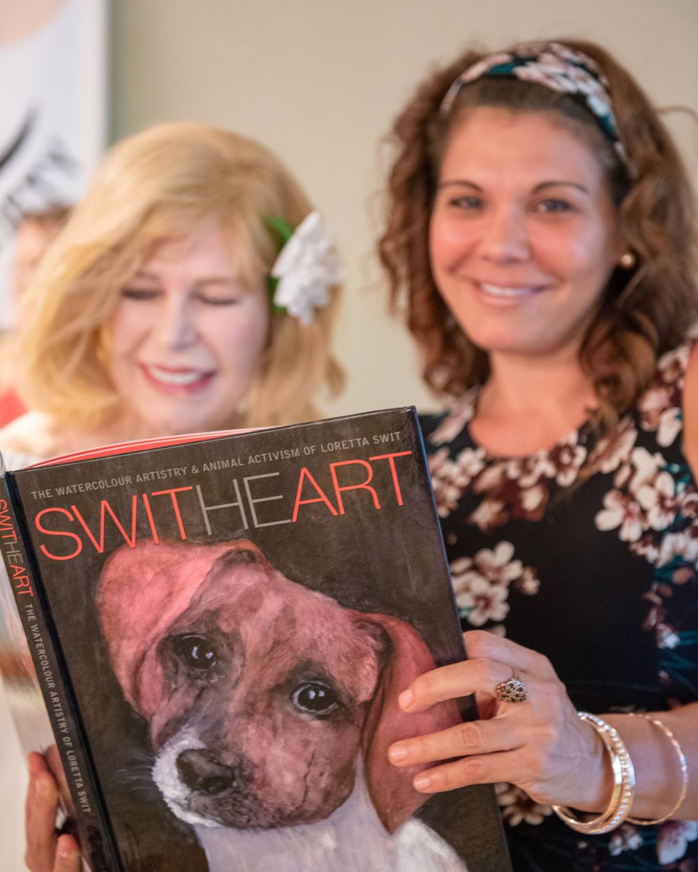 Two attendees at an event holding up a book titled 'Switheart' featuring a dog on the cover.