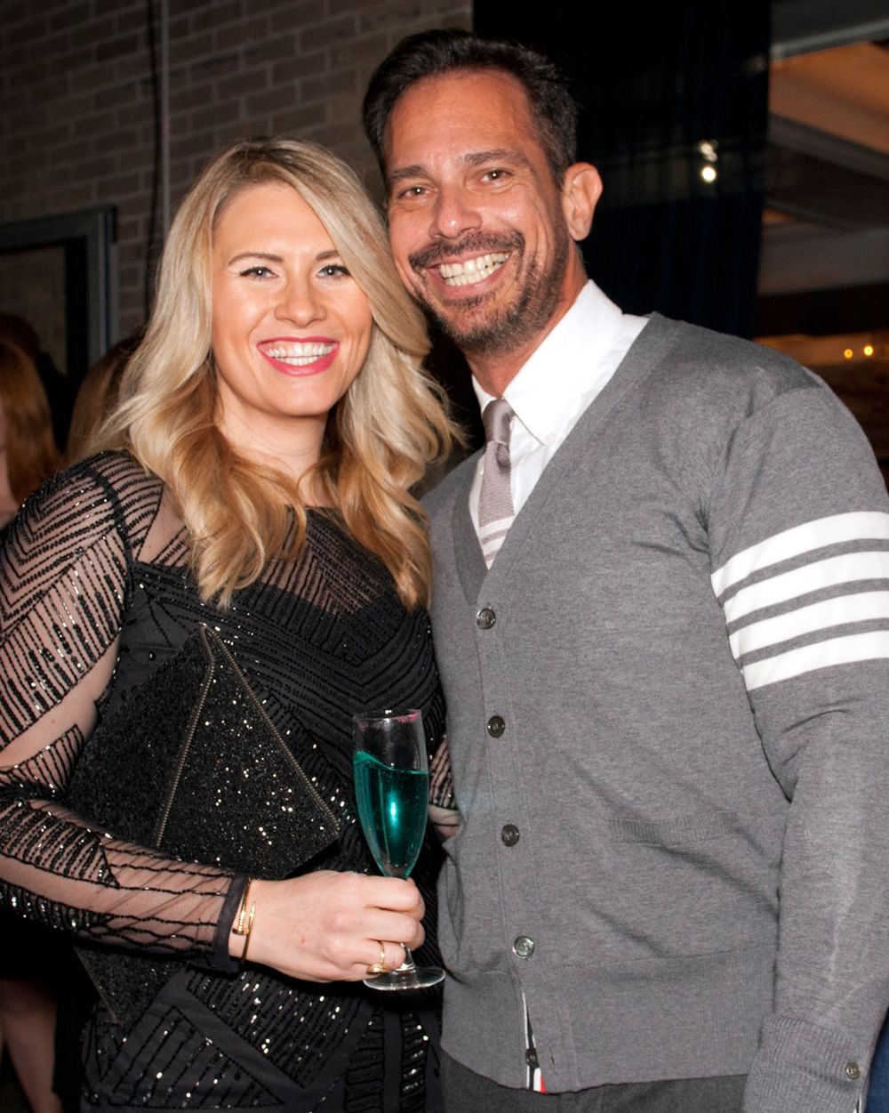 Couple posing at evening event, woman in black sparkly dress and man in grey cardigan.