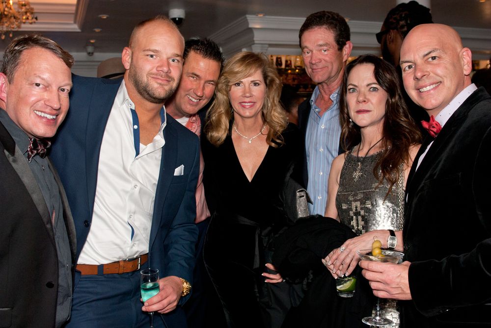 Group of formally dressed people posing together at social gathering with drinks.