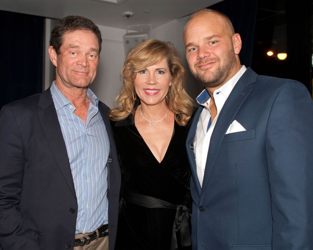 Three people in formal attire pose together at evening event.