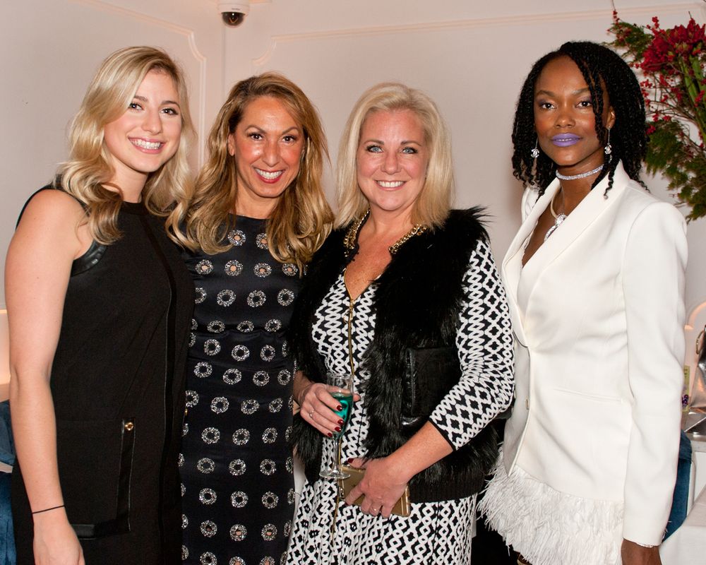 Four women pose together at an elegant event wearing contrasting black, white and patterned cocktail attire.