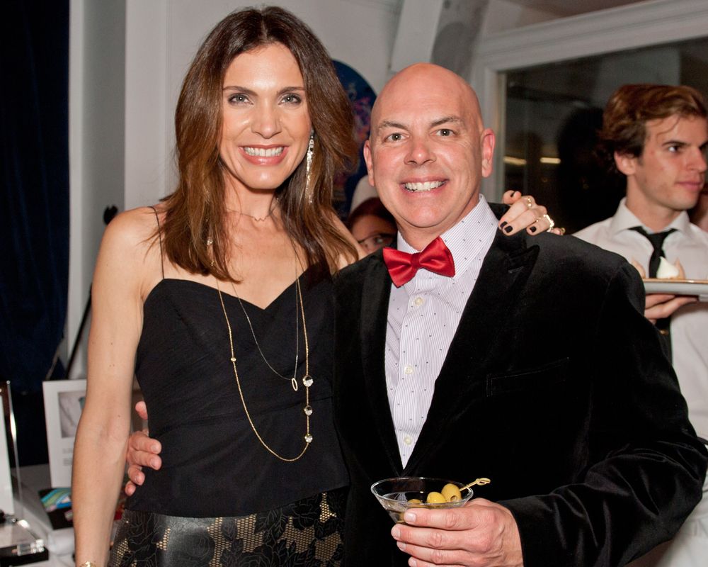 A couple poses together at an event, with the woman in black and the man wearing a red bowtie and velvet jacket.