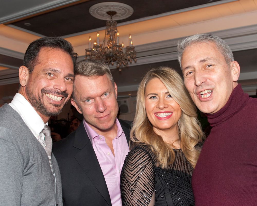 Four people pose together at an elegant event under a chandelier in a formal setting.