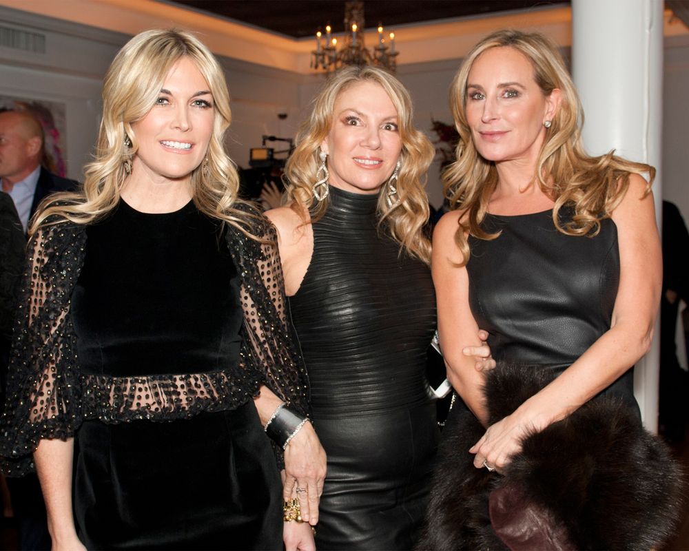 Three women in formal black evening wear pose together at an elegant event.
