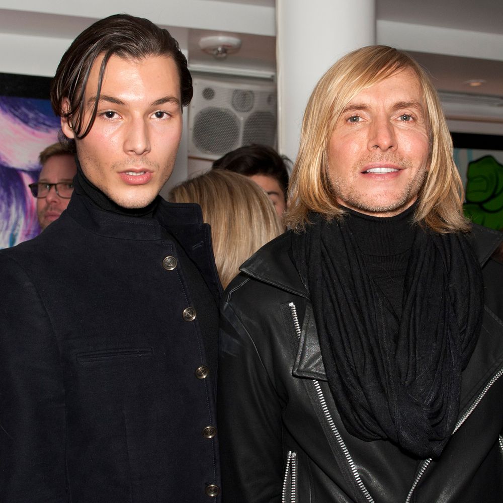 Two people in black turtlenecks pose together at an event with dramatic lighting.
