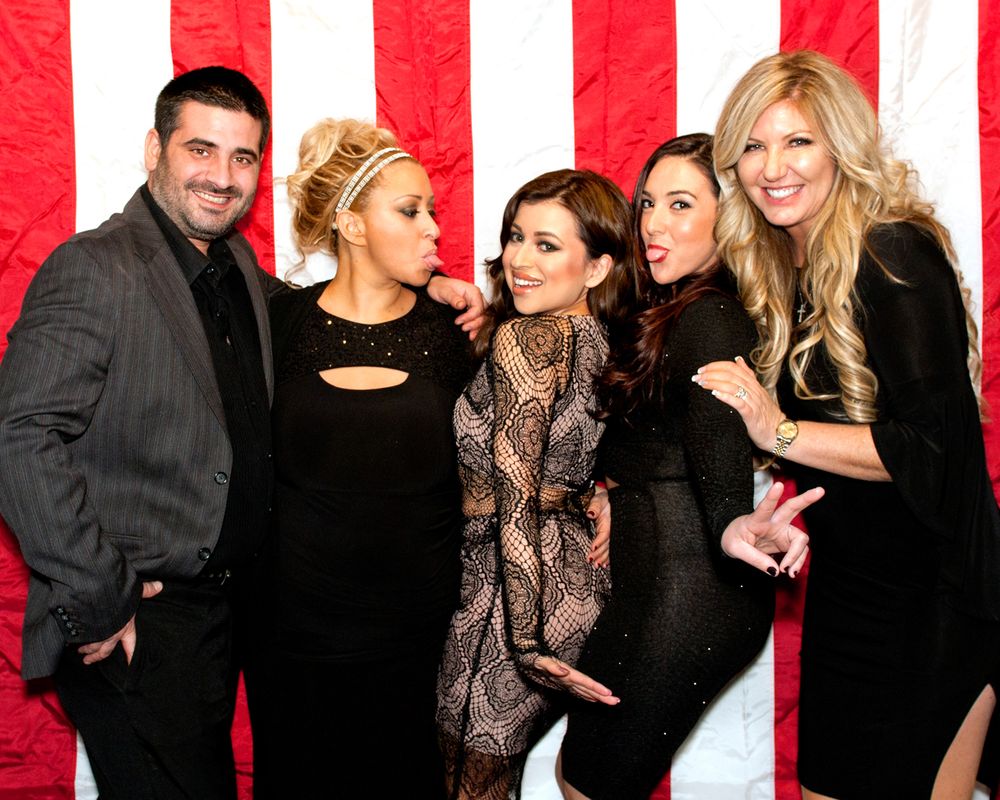 Group photo against red and white striped backdrop at formal gathering wearing black and patterned outfits.