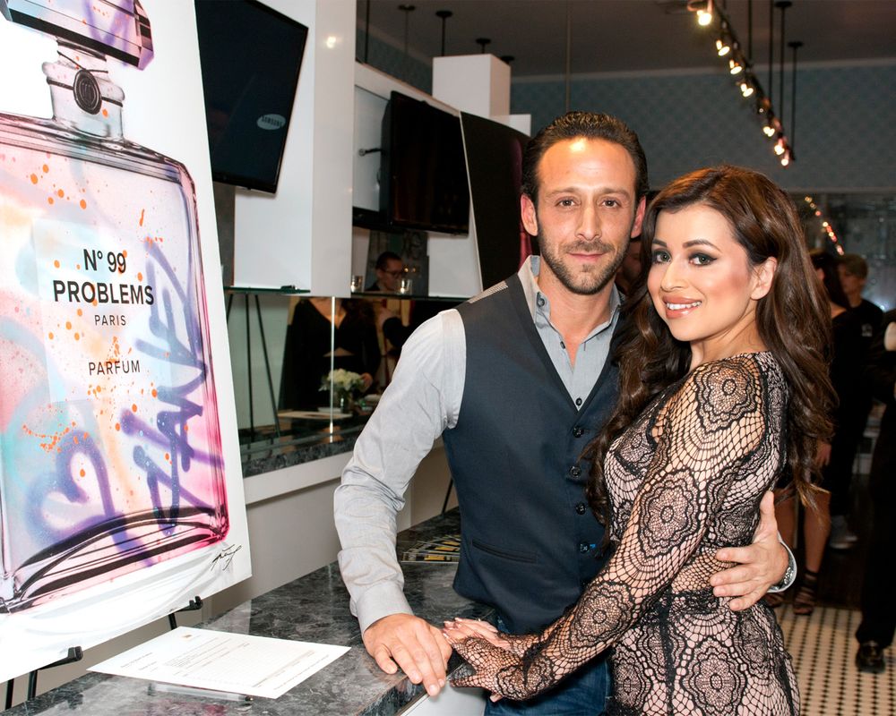 Couple posing together at promotional event with perfume bottle display in background.