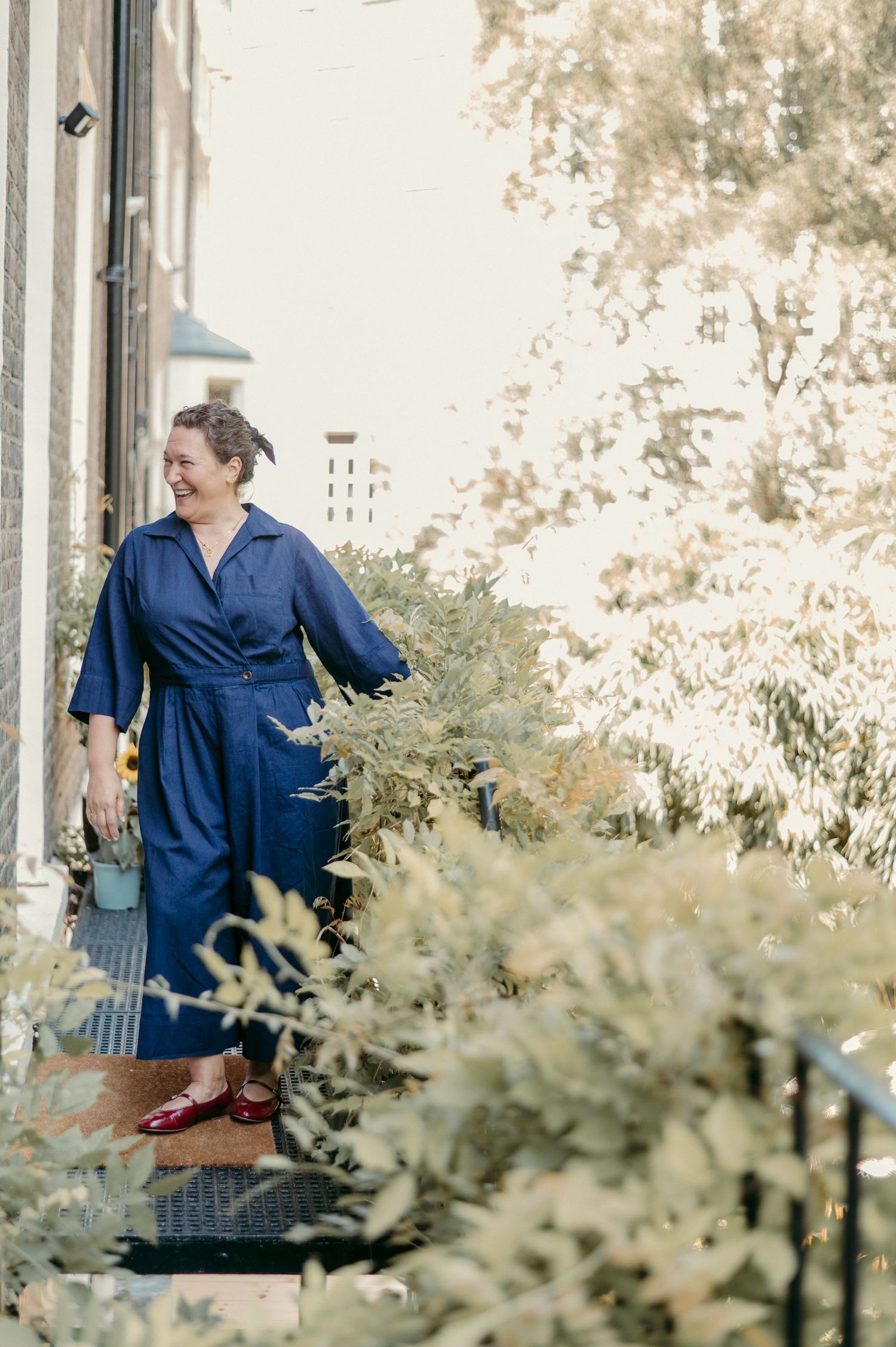 Person in a navy dress standing on porch steps surrounded by lush greenery.
