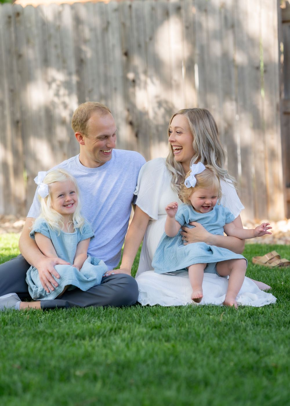 Happy family with young girls in matching blue dresses sitting on grass.