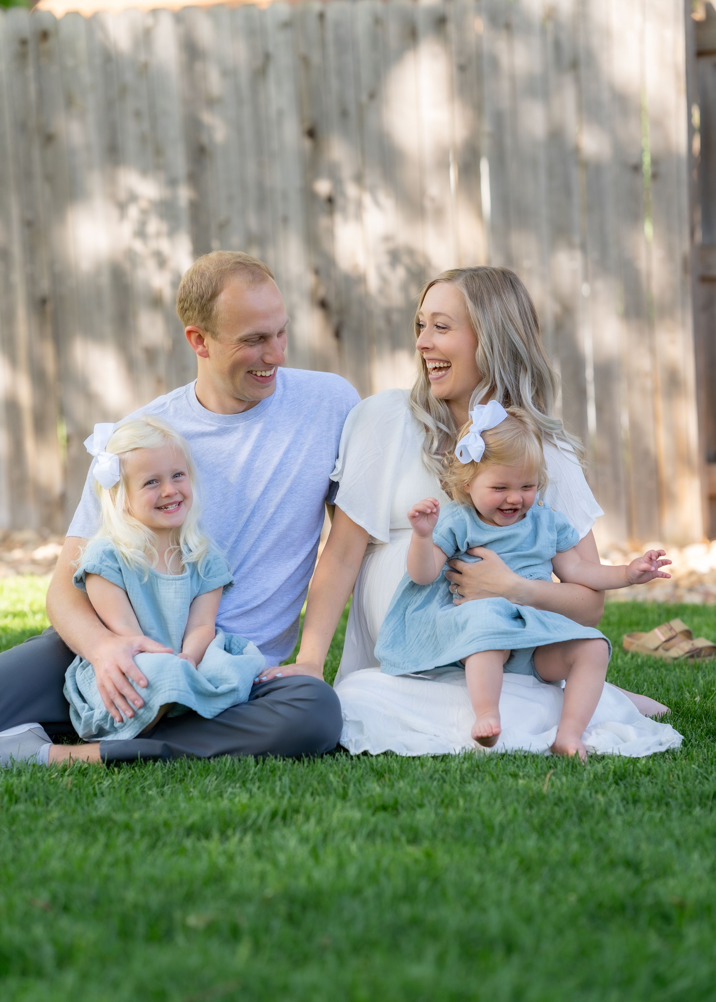 Happy family with young girls in matching blue dresses sitting on grass.