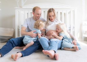 Pregnant mother is embraced by her husband and children while sitting on the floor of their nursery.