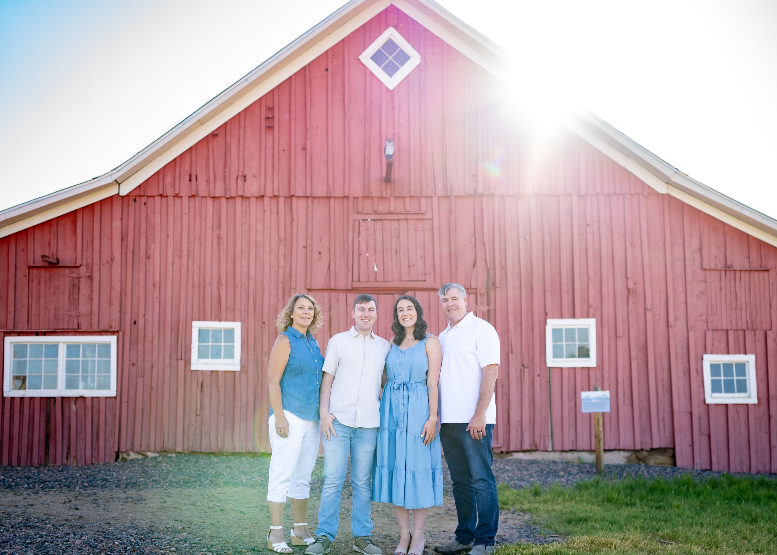 Family of four standing in front of large red barn at sunrise.