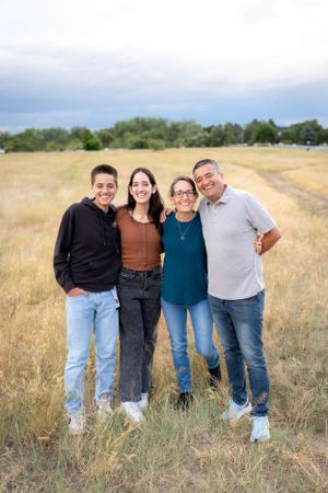 Family of four poses together in casual attire on a grassy hillside field.