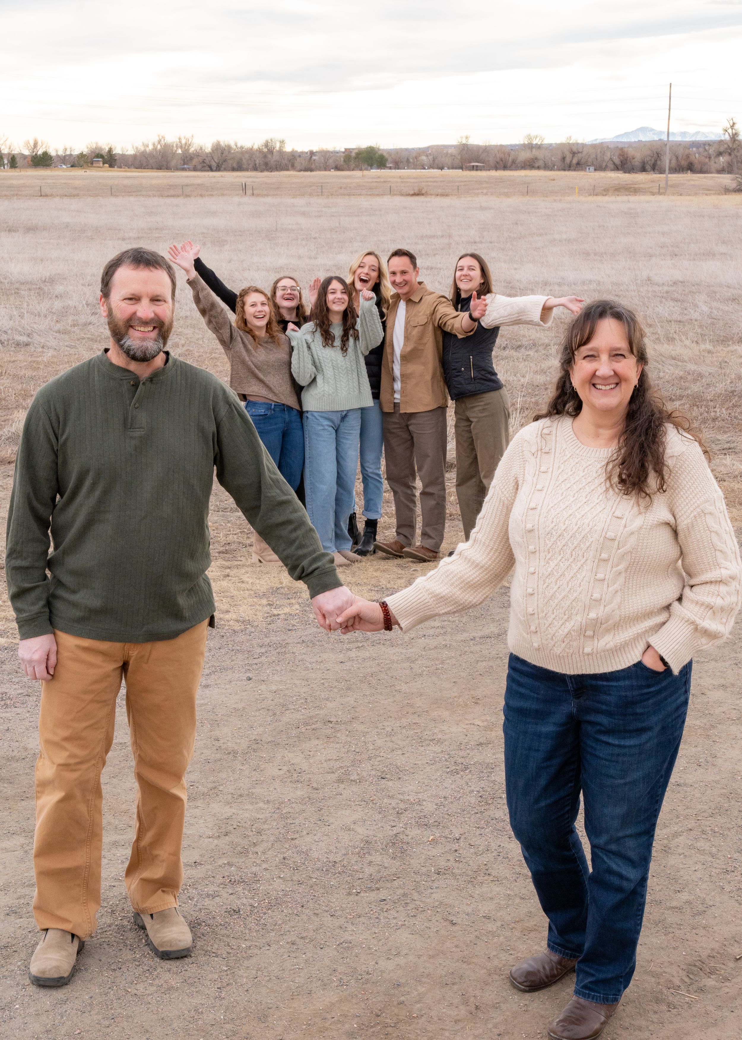 A group poses outdoors in a line formation on a barren field during an autumn day against a backdrop of bare trees.