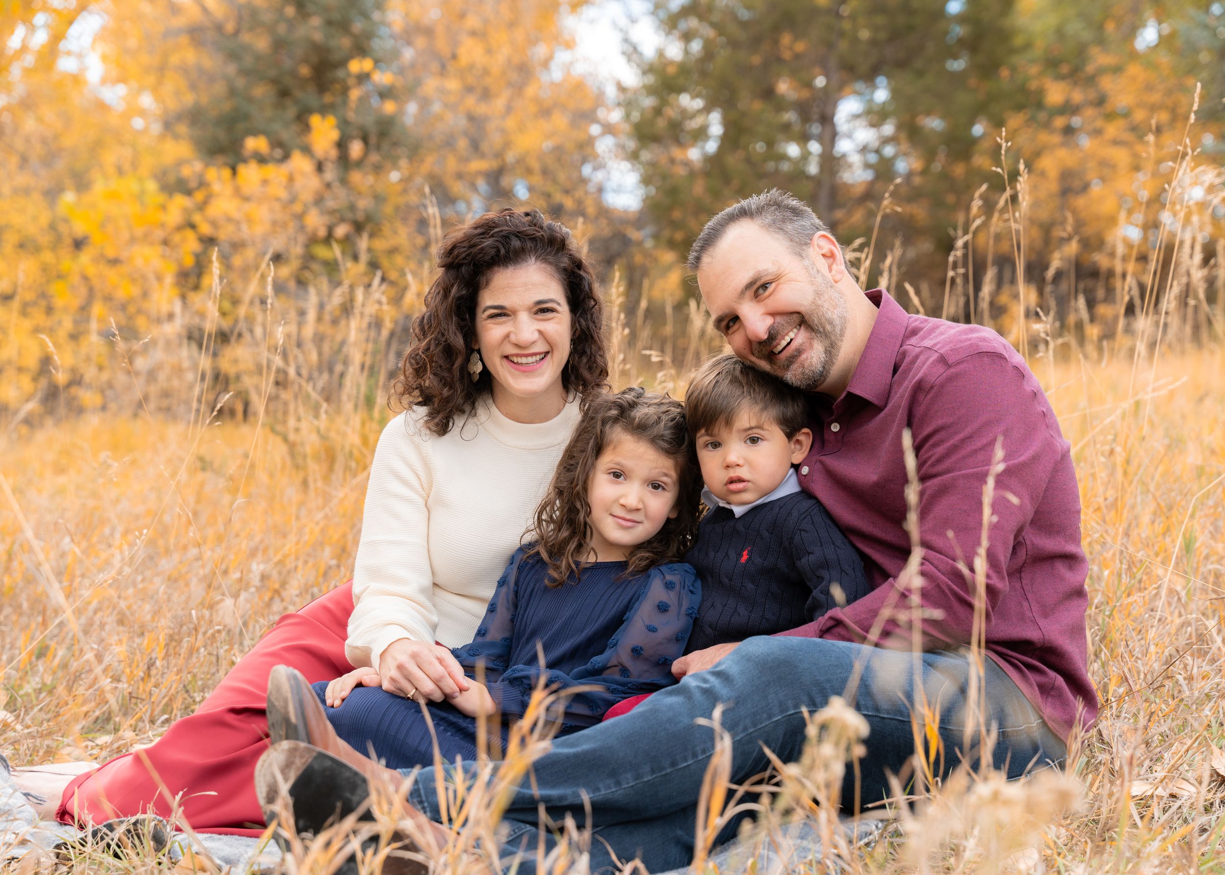 Family of four sitting together in autumn field with golden grass.