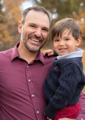 Professional portrait of father and son outdoors with fall foliage in background.