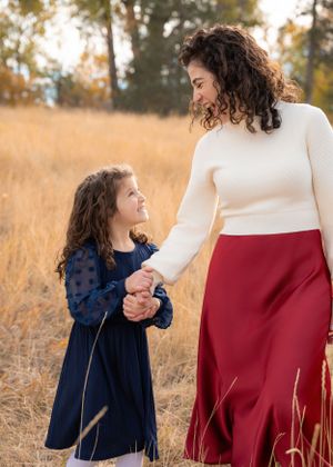 Mother holds hands with her daughter a field of tall golden grass.
