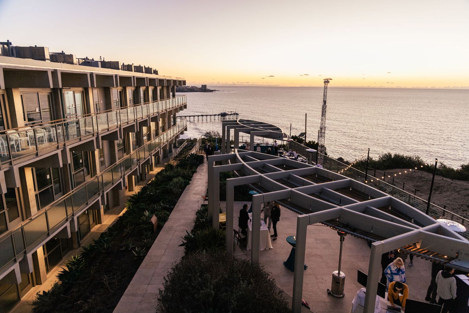Coastal apartment complex with balconies overlooking the ocean at sunset with palm trees in silhouette.