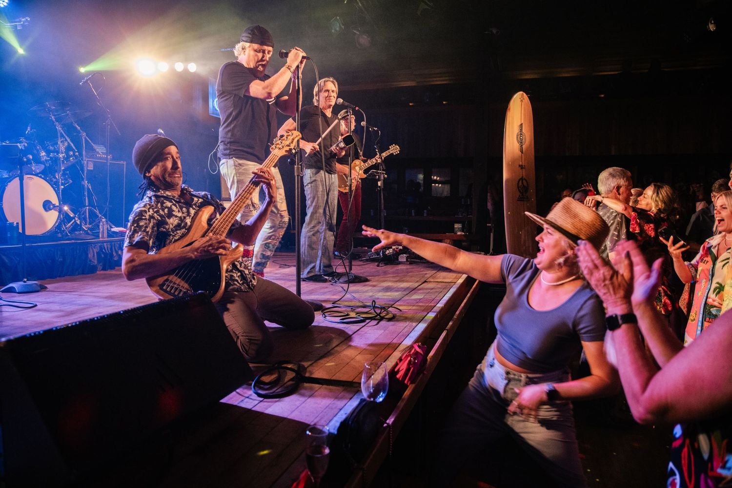 Musicians performing on stage with enthusiastic fans in the crowd at an intimate concert venue.