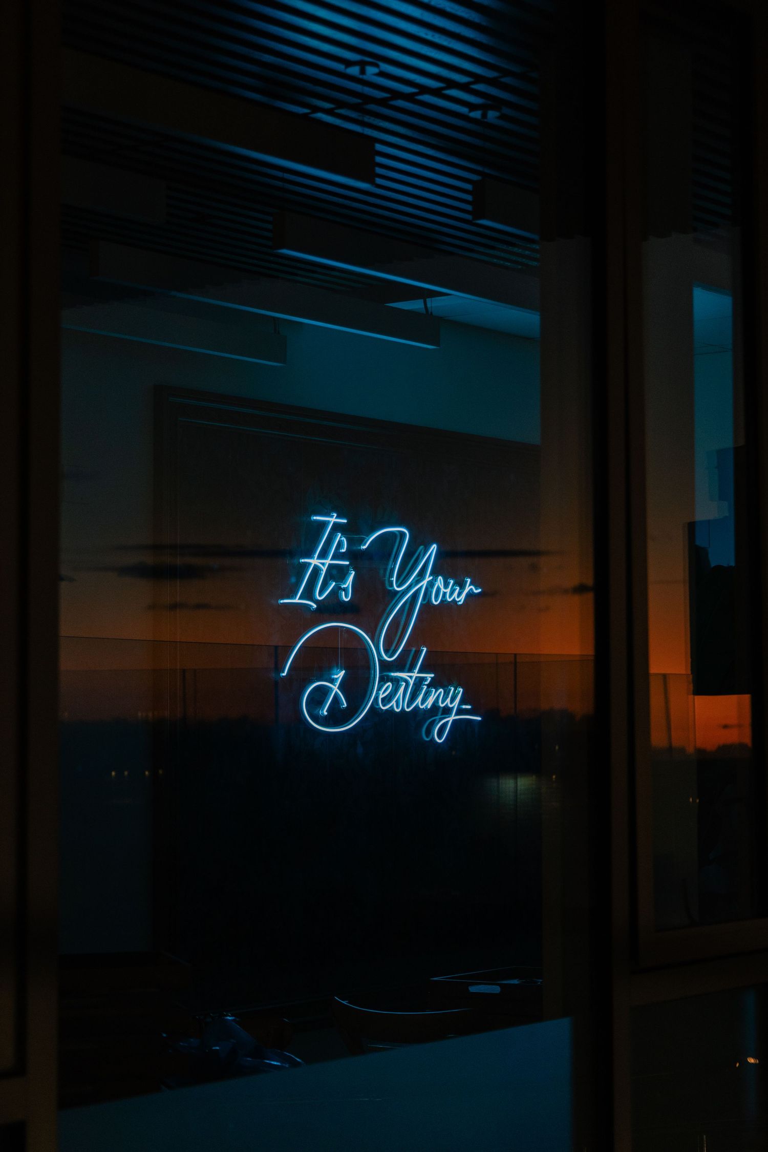 A blue neon sign reading 'It's Your Destiny' glows against a dark window at twilight.