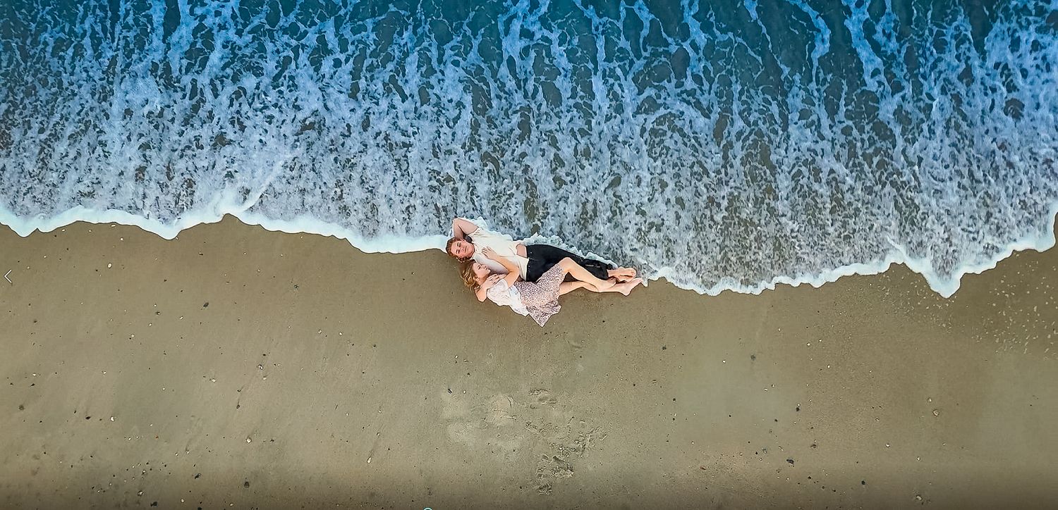 Aerial view of someone laying on sandy beach as ocean waves roll in.
