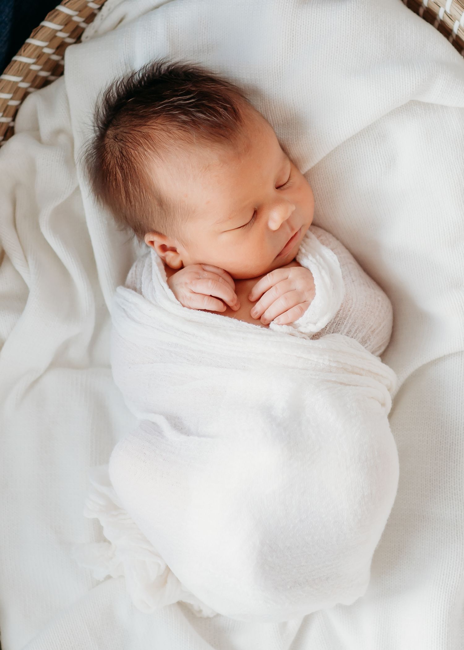 Peaceful sleeping newborn baby swaddled in soft white blankets against white background.