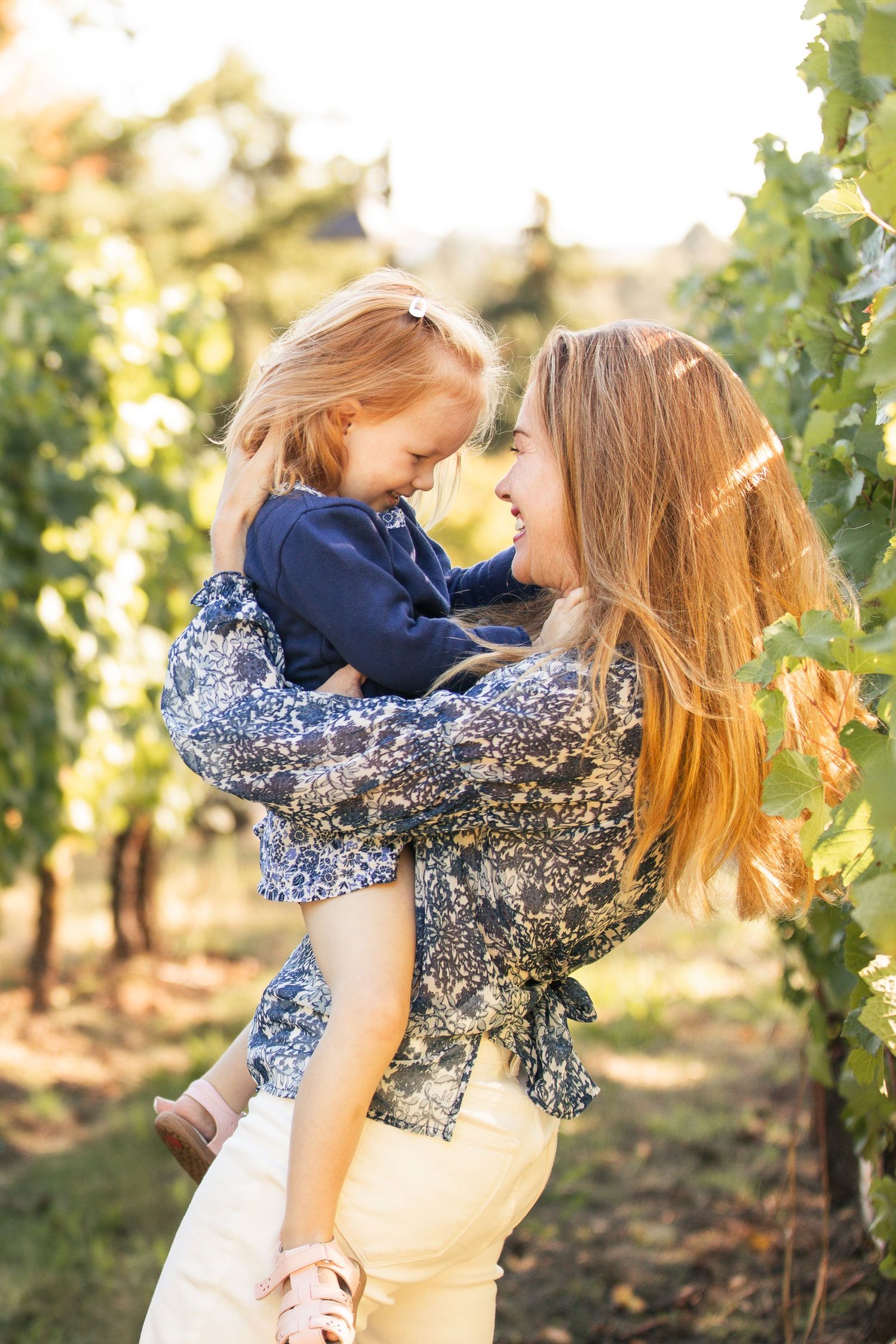 Two people in matching blue floral outfits share a tender moment among vineyard rows at sunset.