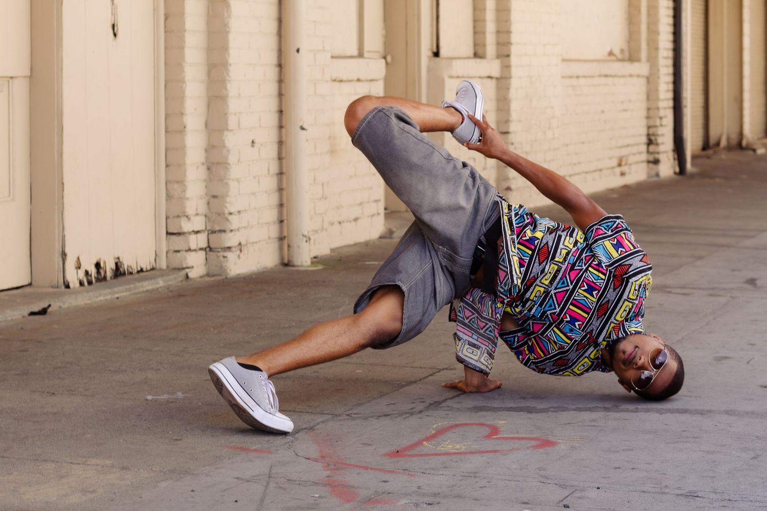 Street dancer in casual clothes and backpack performing breakdance moves on the ground under an urban archway.