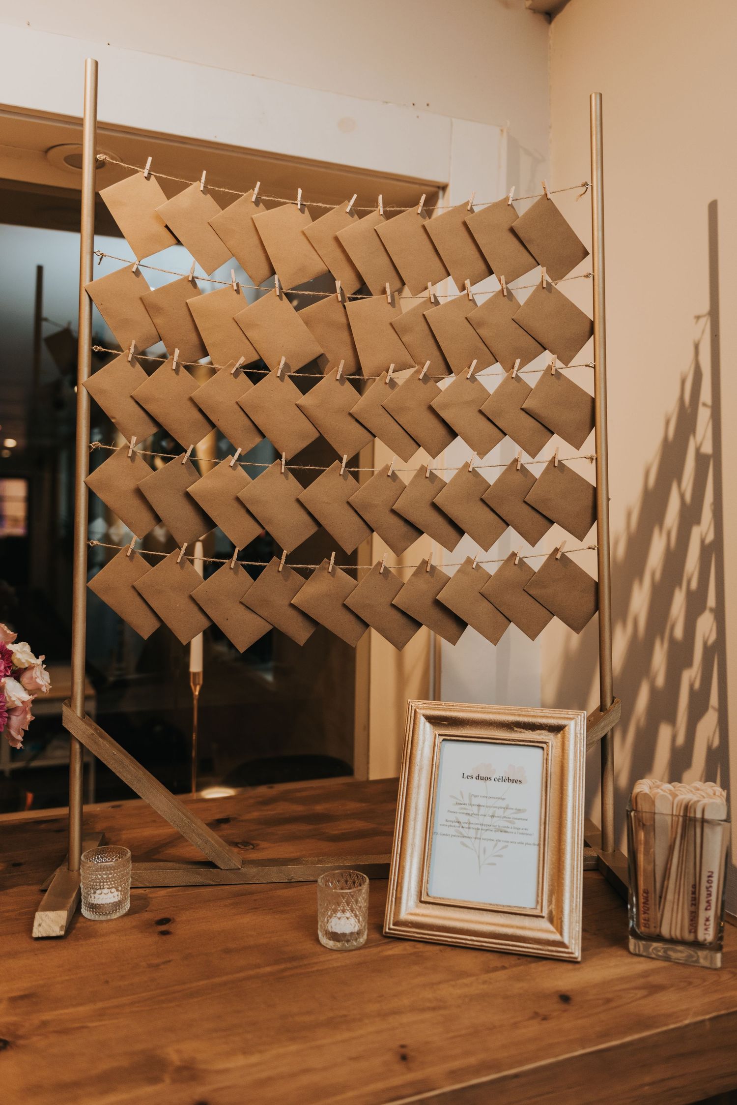 Wedding place cards arranged in diagonal rows on a wooden display with candle holders and framed sign on rustic table.