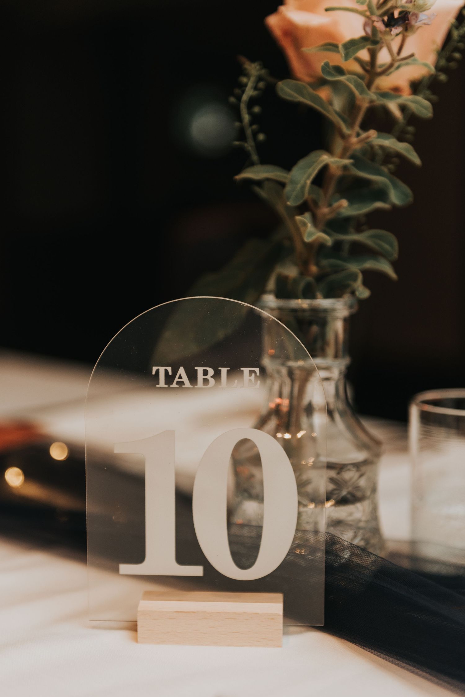 Elegant acrylic table number 10 displayed with greenery in a clear vase at a formal event setting.
